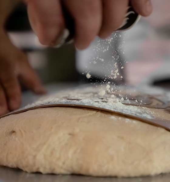 Main déposant de la farine sur une pâte
