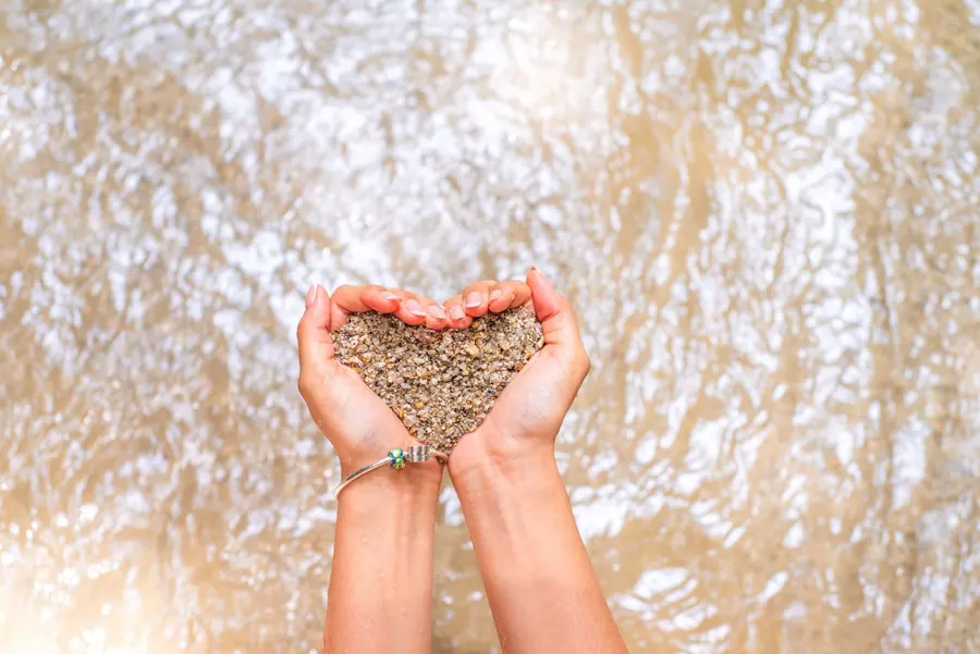 Des mains en coupe forment un cœur de sable et de graviers au-dessus de l'eau vive du Huila.
